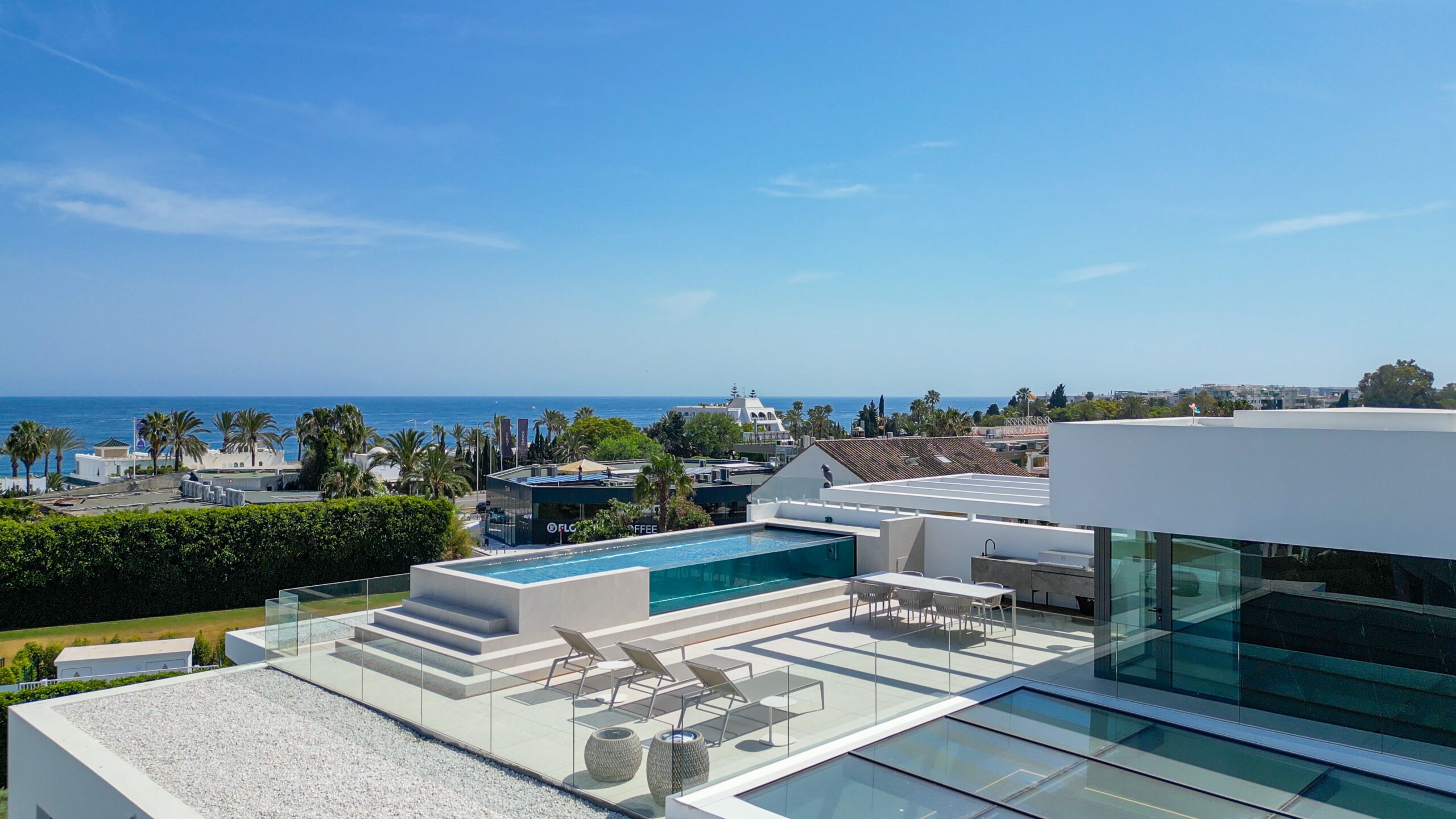 Luxury Estate Broker. Discreet Access. Marbella – La Quinta . Modern coastal terrace with glass railing, lounge chairs, and an infinity pool overlooking the sea.